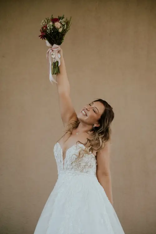 Novia feliz con su vestido blanco de novia alzando el ramo