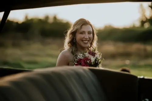 Novia feliz posando a traves de auto en el atardecer