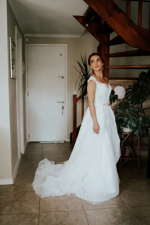 Novia posando feliz con su vestido de novia y su ramo antes de ire de su casa
