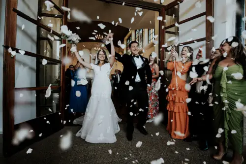 Novios felices saliendo de la iglesia llena de petalos